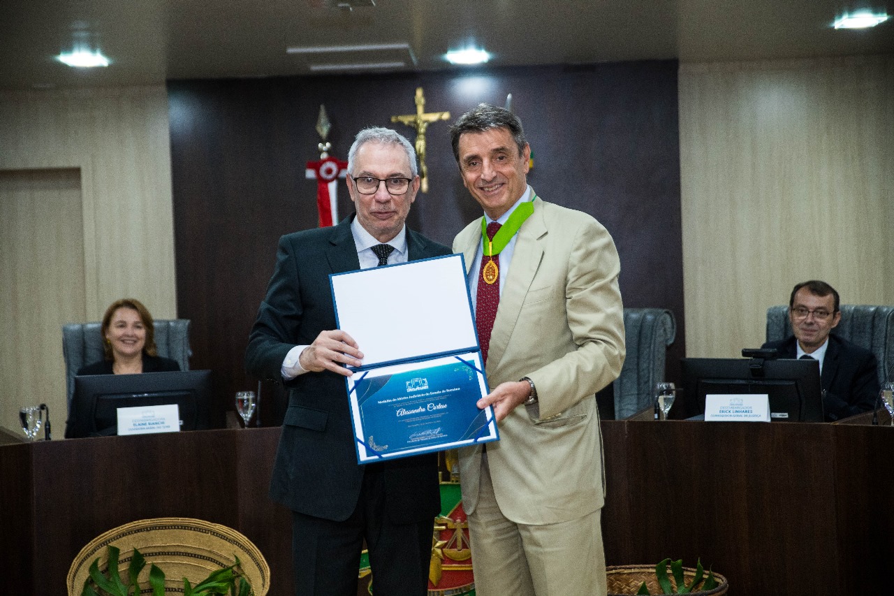 Foto colorida do Alessandro Cortese pousando para fotografia ao lado Desembargador Almiro Padilha. Os dois estão segurando o diploma