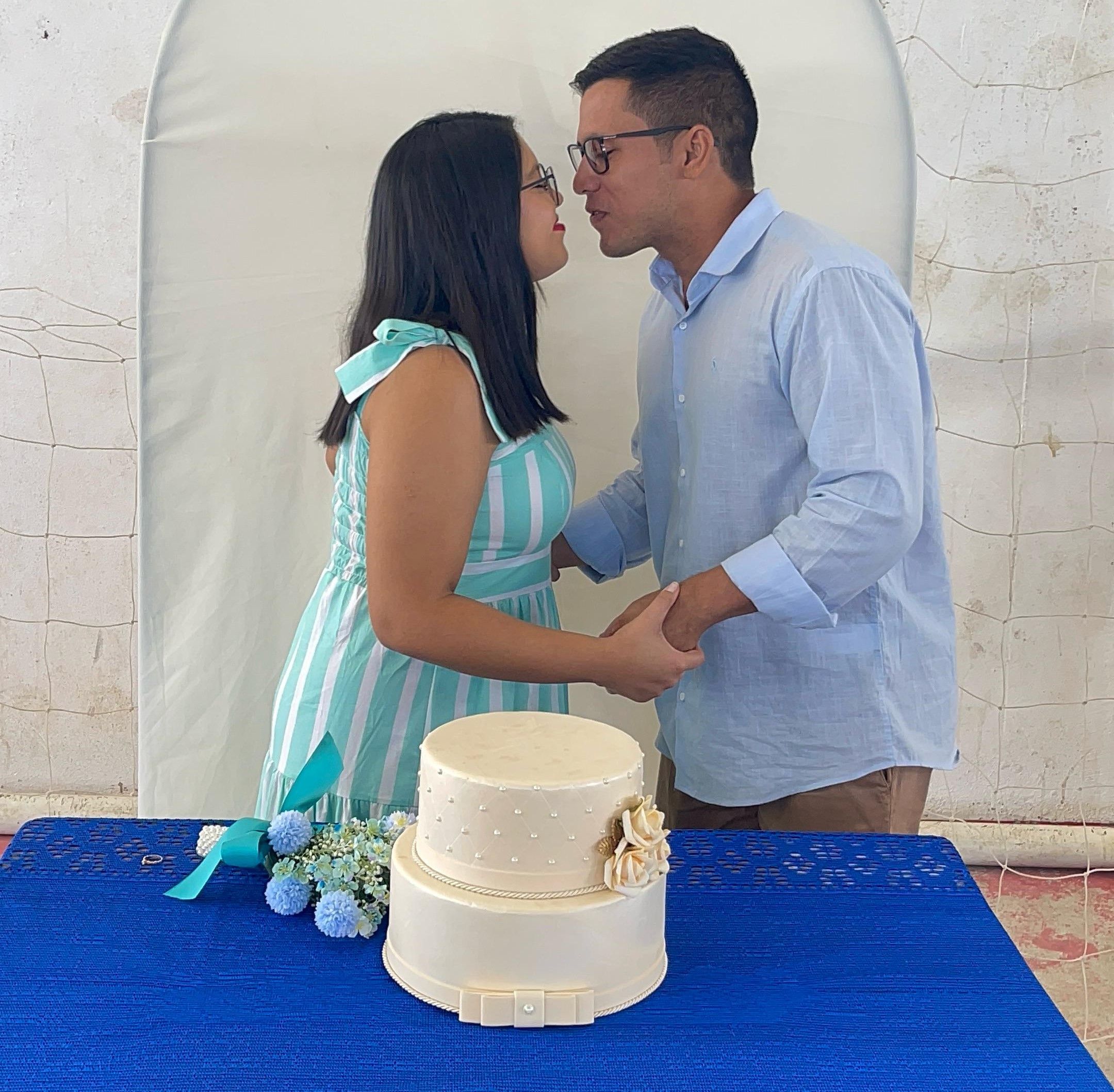 Imagem colorida contém o casal Leandro Leal e Pamela Patricia, se beijando sobre o bolo de casamento, durante ação da Vara da Justiça Itinerante no município de Iracema.