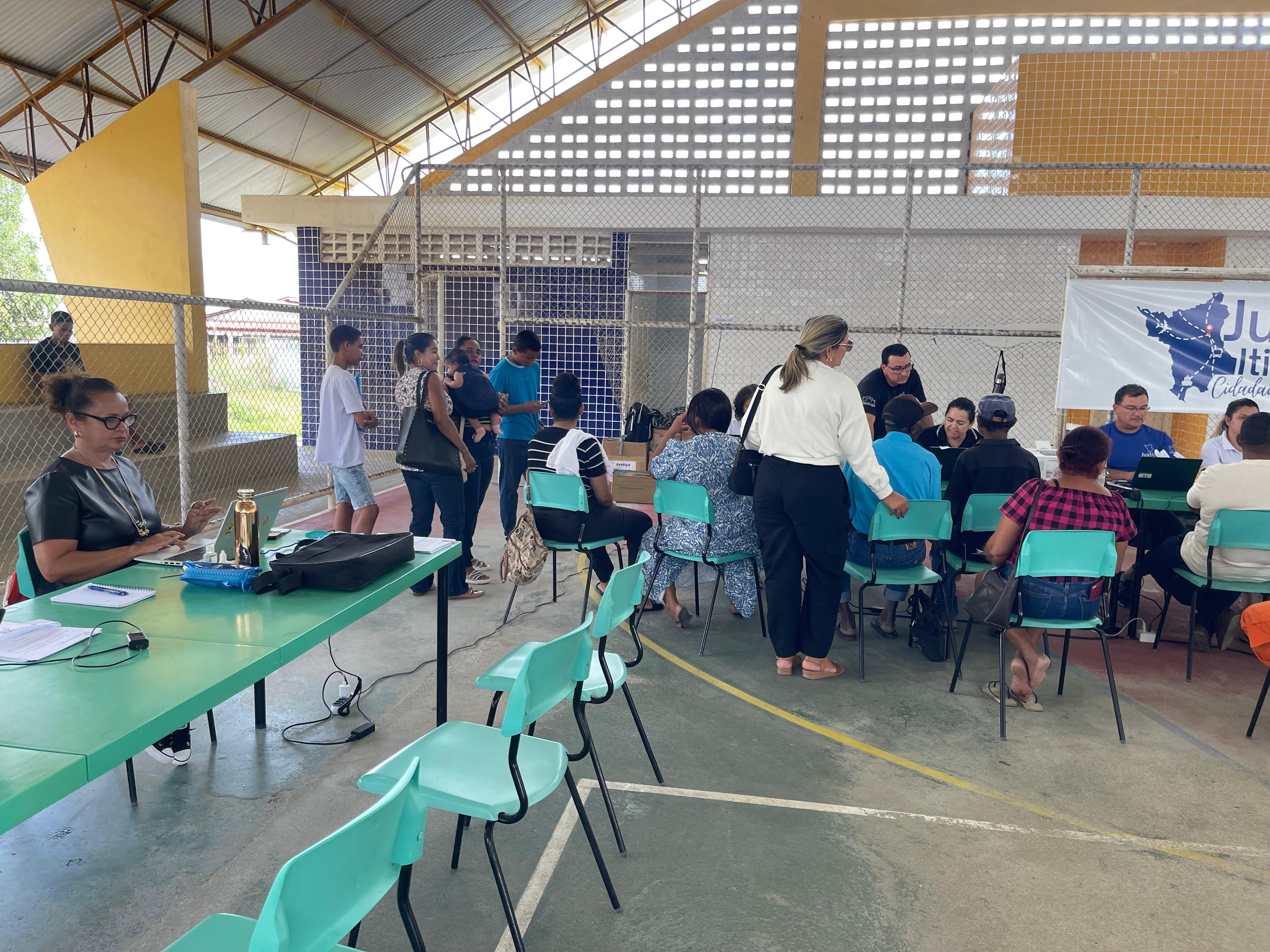 Foto colorida contém a Juíza Titular da Vara da Justiça Itinerante do TJRR, Graciete Sotto Mayor Ribeiro, utilizando notbook, durante ação da Justiça Itinerante em um quadra de escola, no município de Iracema. No segundo plano da imagem logo ao lado da juíza, estão servidores da Vara da Justiça Itinerante atendendo os munícipes que se encontram sentados à frente dos servidores.