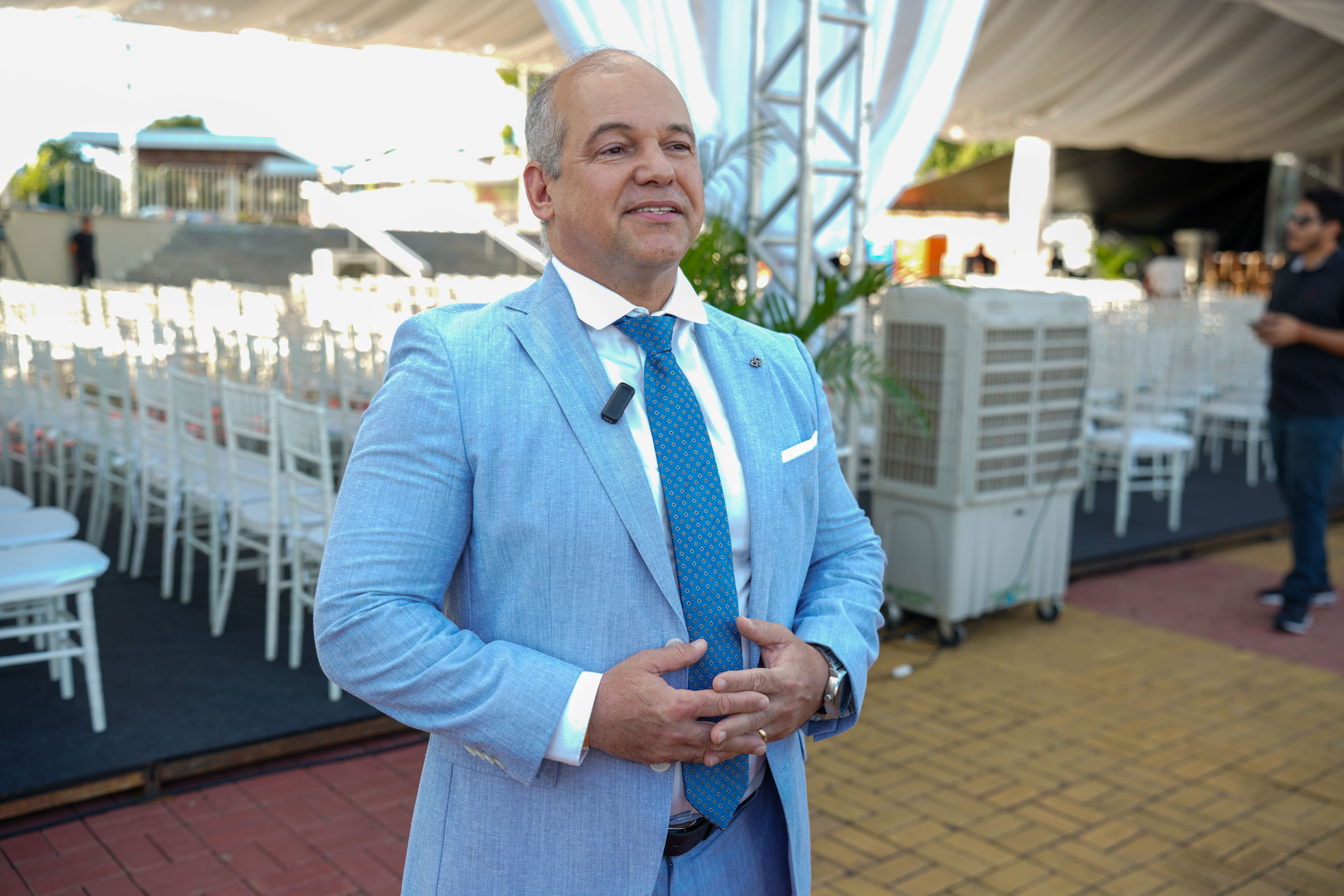 Foto colorida mostra o juiz auxiliar da Corregedoria Eduardo Alvares de Carvalho. vestido com um terno azul-claro e uma gravata azul-escura com bolinhas brancas, sorrindo enquanto concede uma entrevista. Ele está ao ar livre, com cadeiras brancas visíveis ao fundo. Foto colorida mostra o juiz auxiliar da Corregedoria Eduardo Alvares de Carvalho. vestido com um terno azul-claro e uma gravata azul-escura com bolinhas brancas, sorrindo enquanto concede uma entrevista. Ele está ao ar livre, com cadeiras brancas visíveis ao fundo.