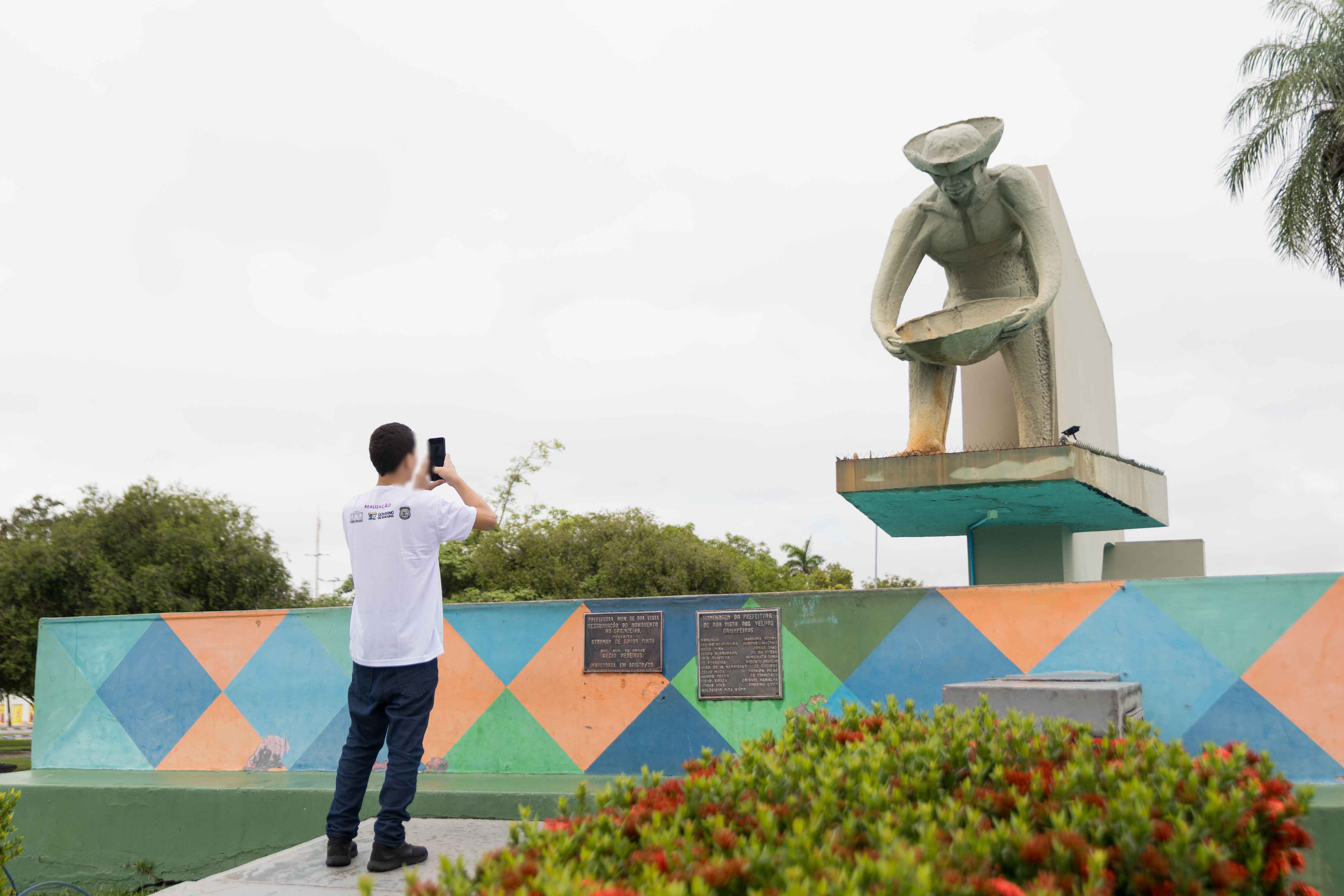 Foto colorida contém adolescente de costas fotografando o Monumento do Garimpeiro, localizado no Centro da Capital Boa Vista, Roraima. Foto colorida contém adolescente de costas fotografando o Monumento do Garimpeiro, localizado no Centro da Capital Boa Vista, Roraima.