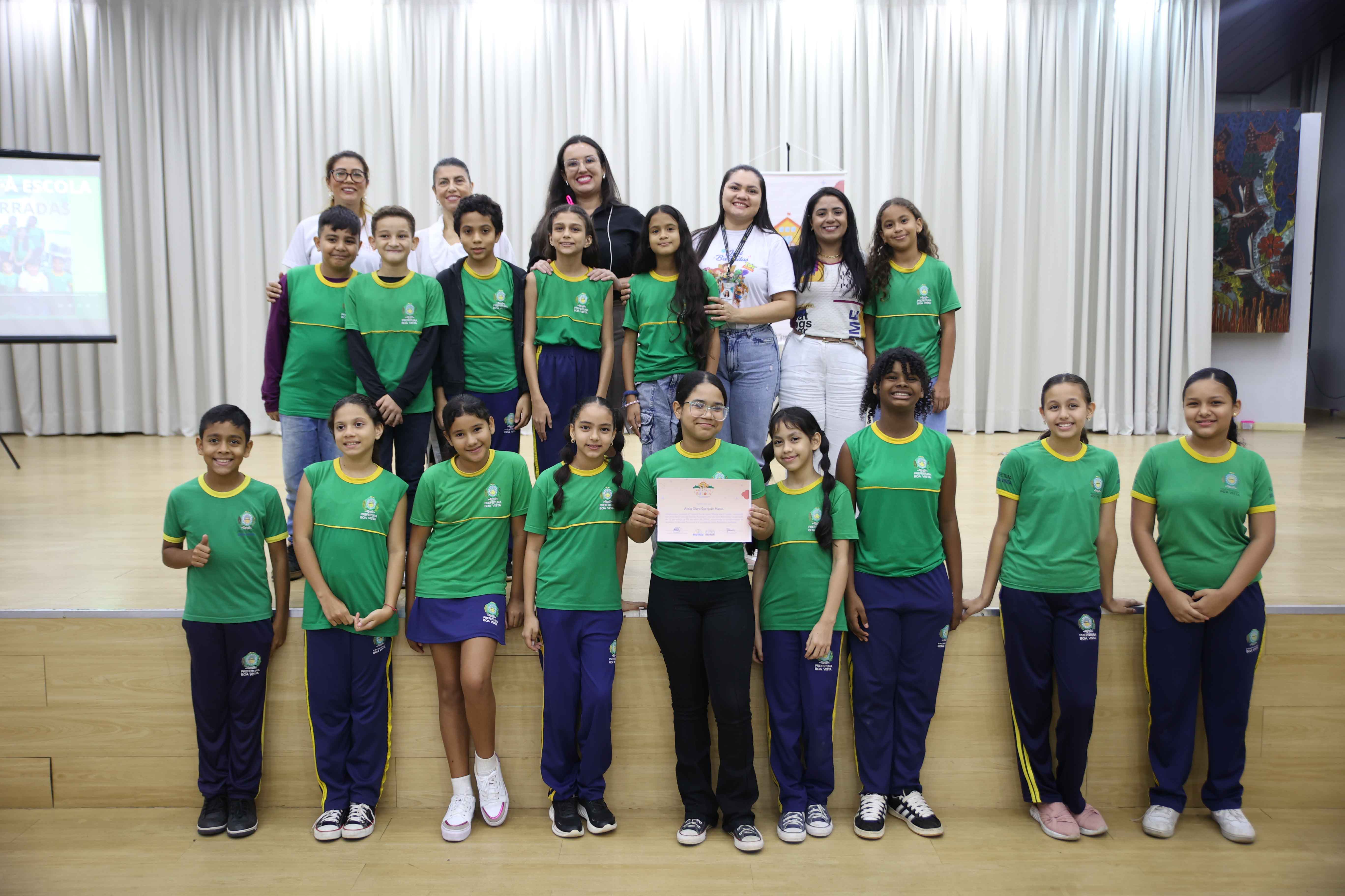  Foto colorida contém a juíza Suelen Alves, coordenadora da Coordenadoria Estadual da Mulher em Situação de Violência Doméstica (Cevid/TJRR), posando para fotografia ao lado de criança segurando certificado do Maria Vai à Escola. 