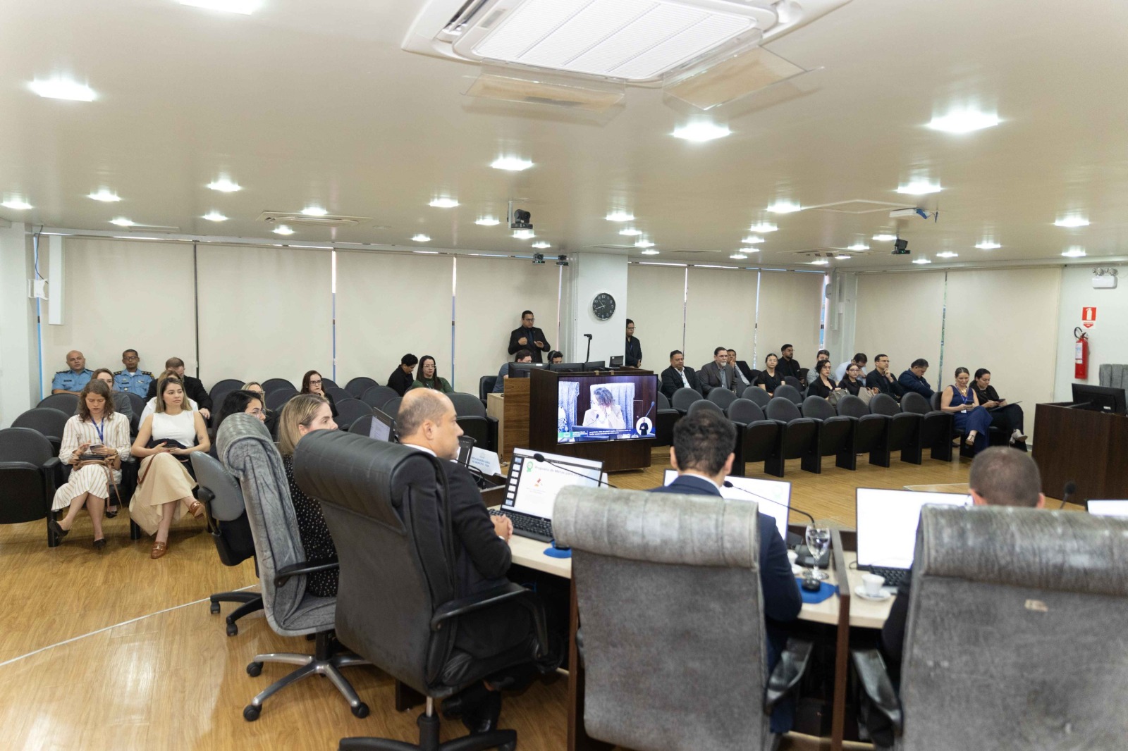 Grupo de 13 pessoas em pé, lado a lado, posando para foto em uma sala de plenário. Ao fundo, telas mostram o texto “Audiência Pública”. Grupo de 13 pessoas em pé, lado a lado, posando para foto em uma sala de plenário. Ao fundo, telas mostram o texto “Audiência Pública”.